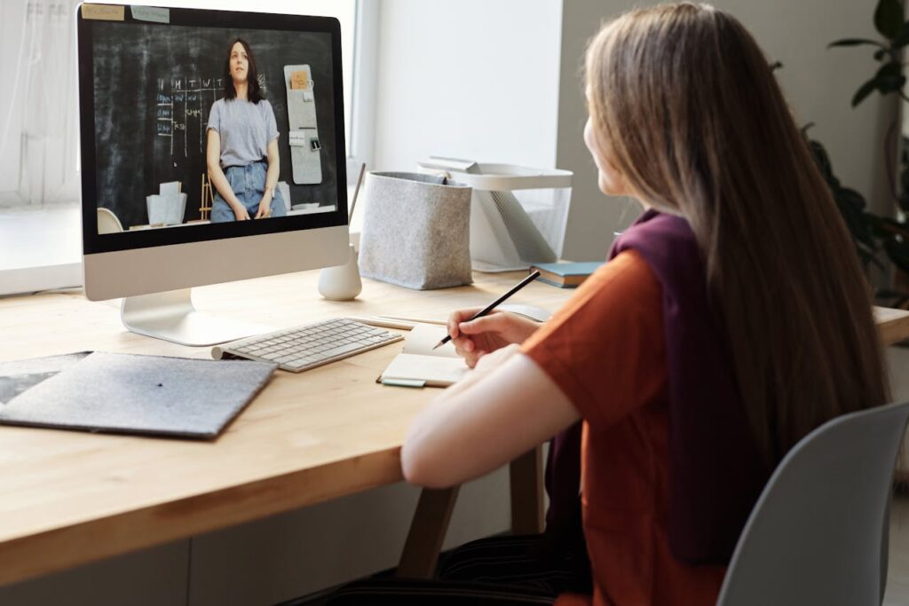 Teen girl attending an online class at home, takes notes at her desk.